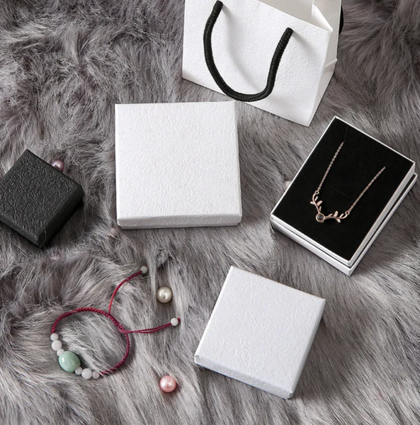 Jewelry including a necklace and bracelet on a fur surface with white boxes and a shopping bag.