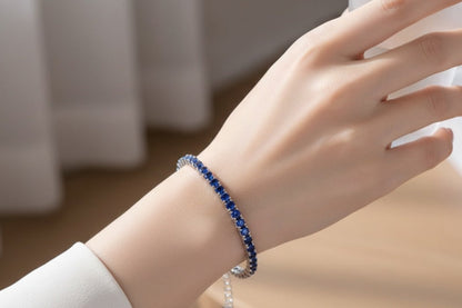 Hand wearing a blue tennis bracelet with a blurred background